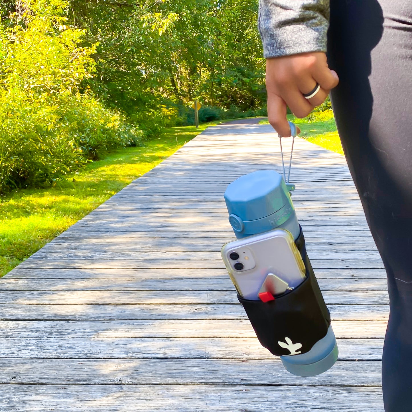 A girl holding a water bottle with a phone pouch sleeve on a hiking trail.