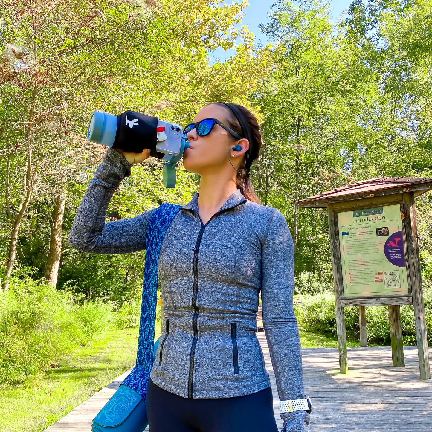 A girl drinking out of a water bottle with a phone pouch while hiking