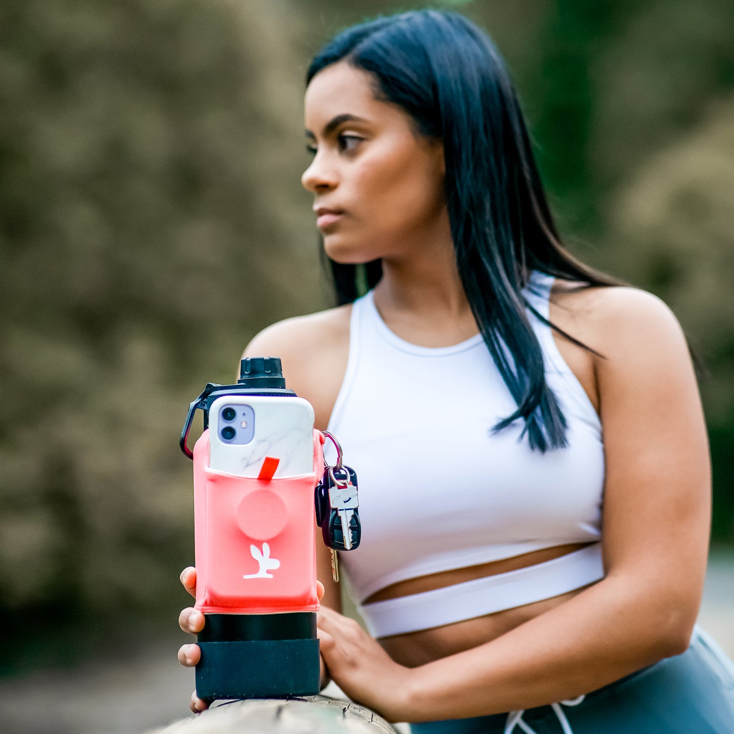 A woman is holding a gym bottle with a peach phone pouch.