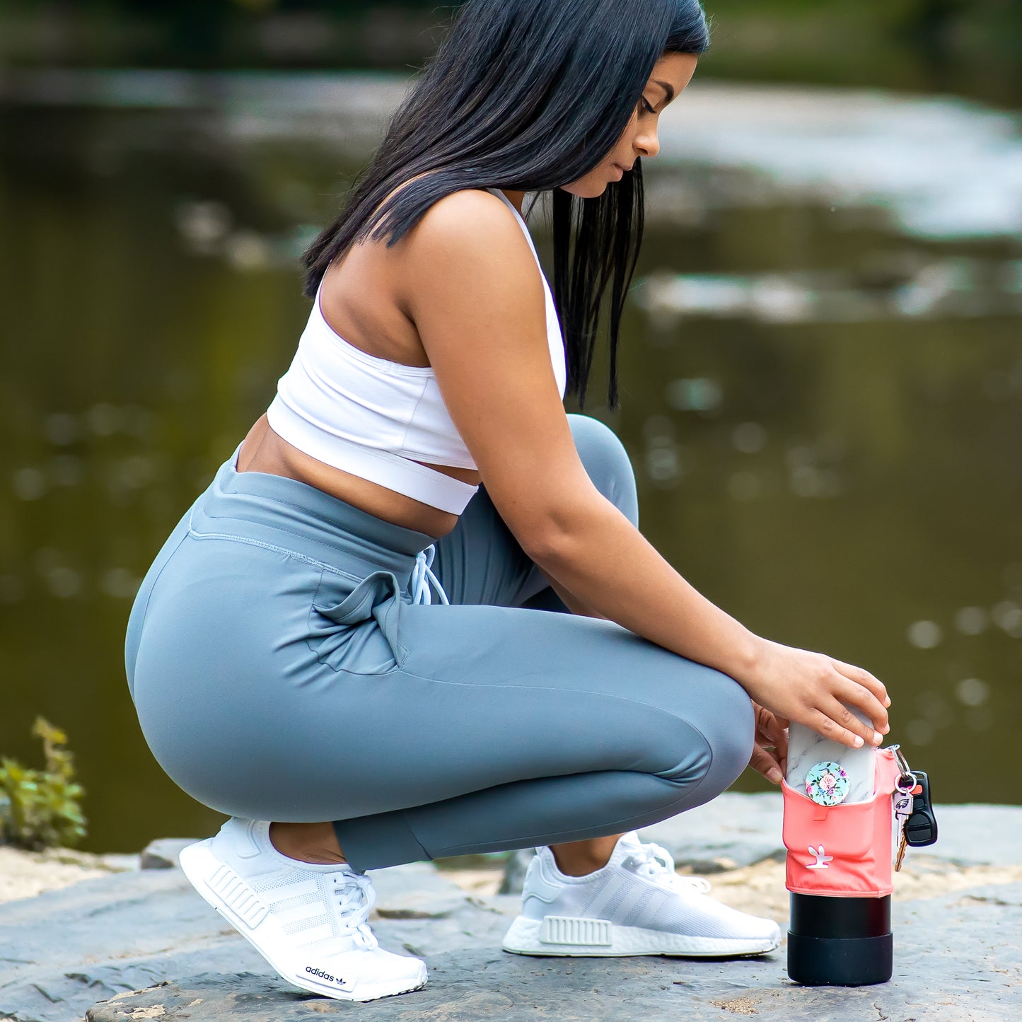 She is on a river bank putting her phone into a water bottle phone pocket.