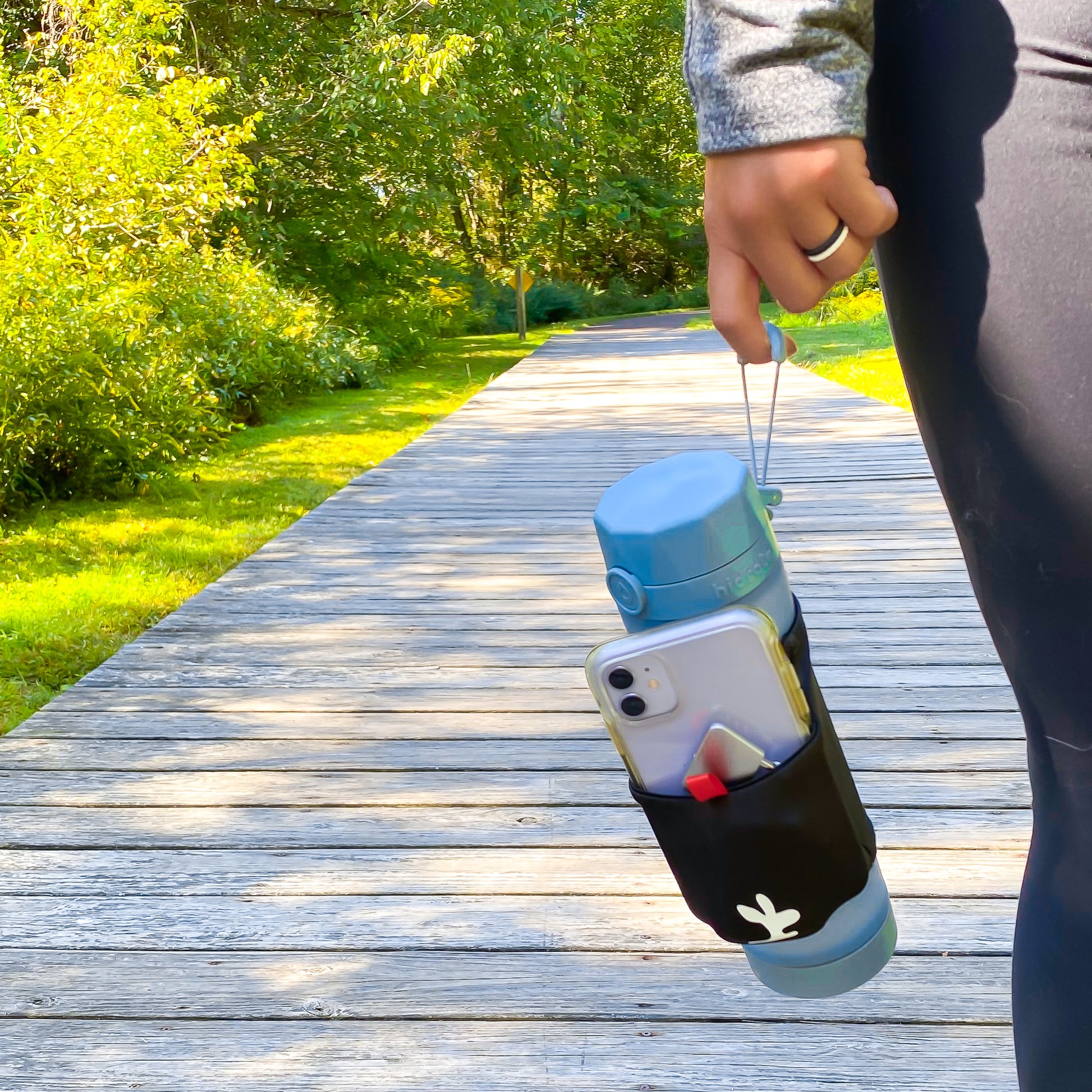 A girl holding a water bottle with a phone pouch sleeve on a hiking trail. 