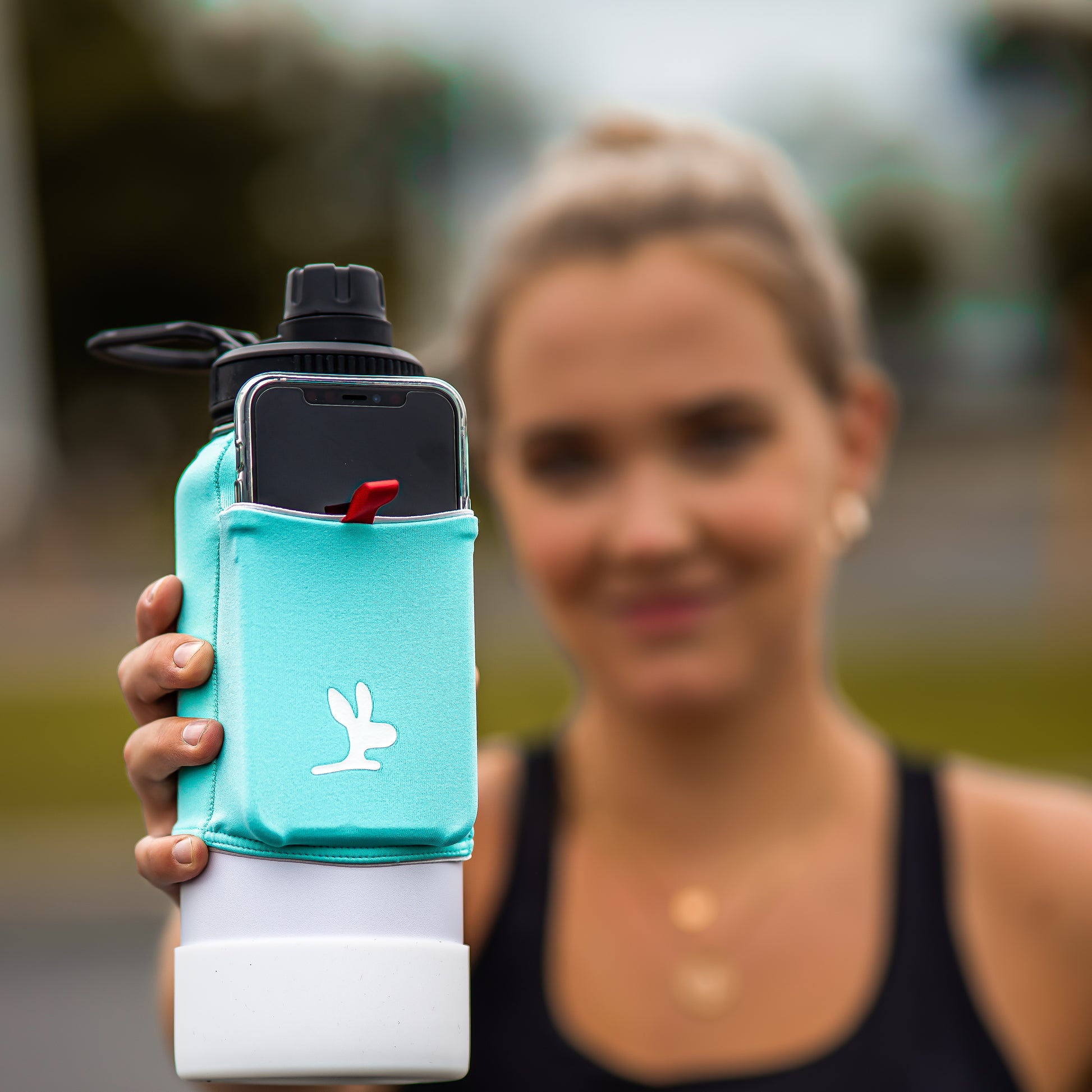 A girl holding a water bottle with a teal phone holder 