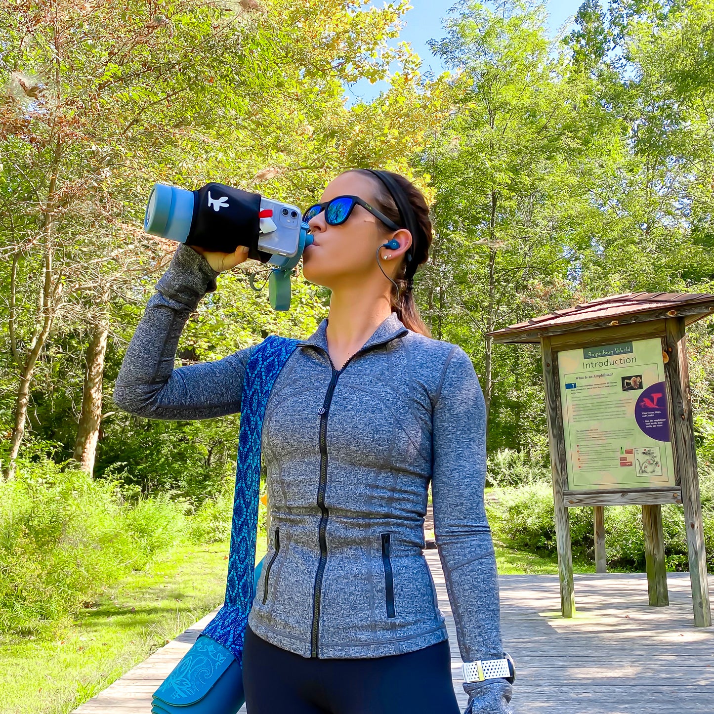 A girl drinking out of a water bottle with a phone pouch while hiking