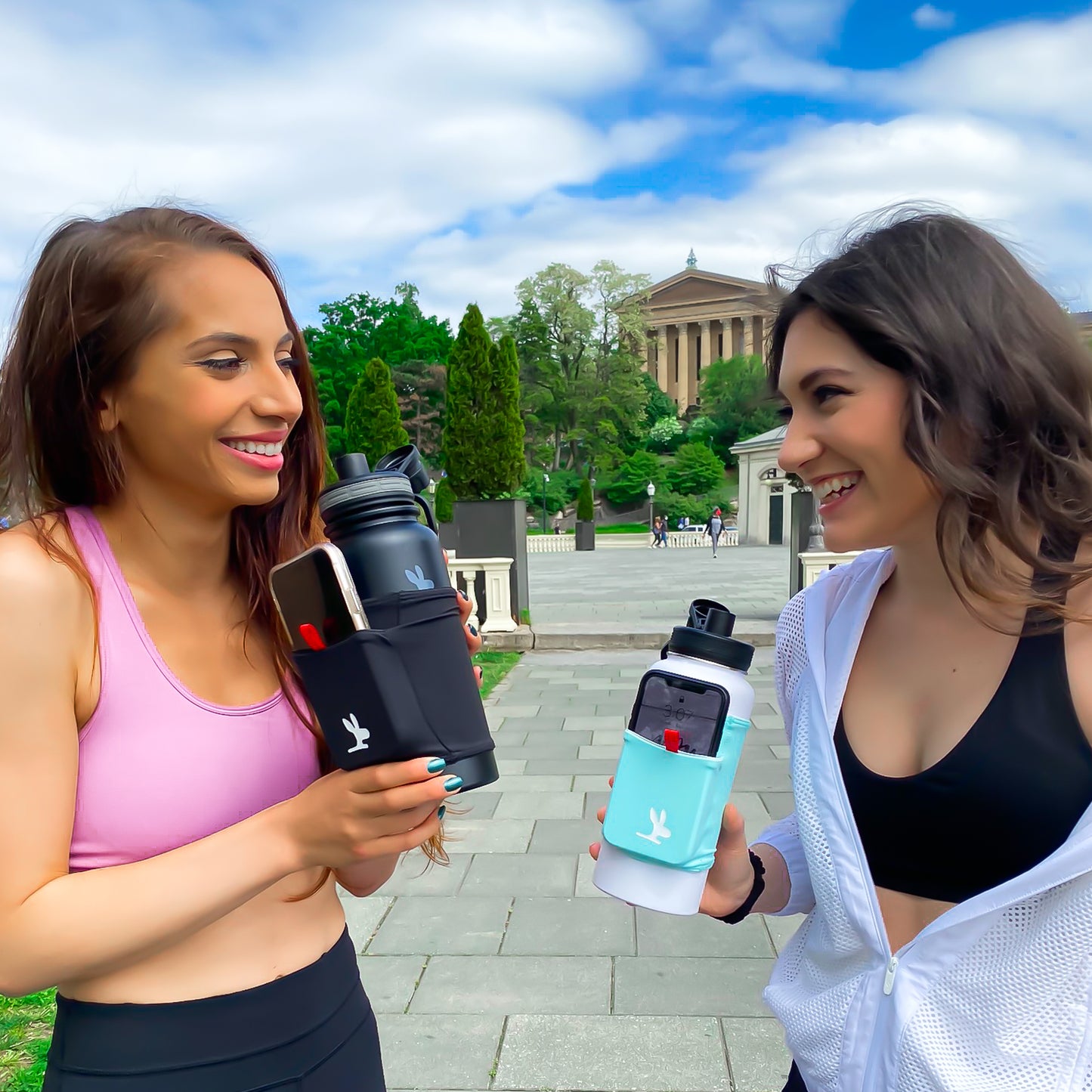 Two girls smiling holding water bottles with a phone hold holder sleeve on them.